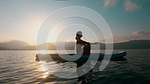 Unrecognizable woman practicing yoga on SUP board at sunset in slow motion