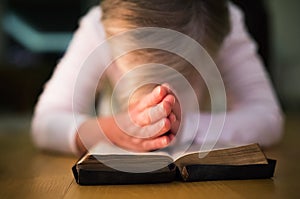 Unrecognizable woman praying, hands clasped together on her Bibl