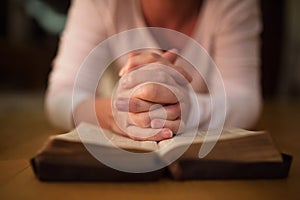 Unrecognizable woman praying, hands clasped together on her Bibl