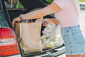 Unrecognizable woman put her shopping eco bags with food into car trunk on a parking.