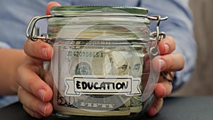 Unrecognizable woman put on table Saving Money In Glass Jar filled with Dollars banknotes. EDUCATION transcription in