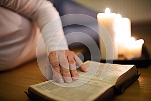 Unrecognizable woman reading Bible. Burning candles next to her.