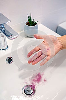Unrecognizable woman removing glitter of her hand into washbasin and polluting clean water