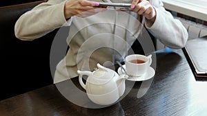 Unrecognizable woman`s hands pictures of teapot and Cup in a cafe on her cell phone. Front view.