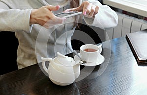 Unrecognizable woman`s hands pictures of teapot and Cup in a cafe on her cell phone. Side view.