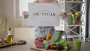 Unrecognizable woman showing Go vegan standing at table with healthful food. Young slim Caucasian millennial lady