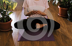 Unrecognizable woman is sitting in  lotus position on  yoga mat and using  mobile phone. Yoga and meditation applications, new