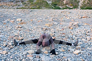 Unrecognizable woman stretching on the pebble shore. Dressed in a jacket, leggins and sneakers.