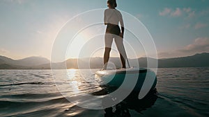Unrecognizable woman at summer sunset sea surfing on a SUP board.
