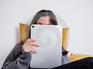Unrecognizable woman using a silver digital tablet and lying on a bed