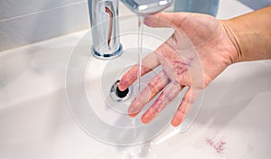 Unrecognizable woman washing glitter of her hand into basin at bathroom and polluting clean water