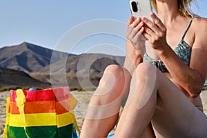 Unrecognizable woman wearing a hat sitting on the beach and using a smartphone