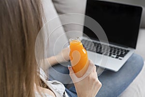 Unrecognizable woman working on laptop and drinking detox orange juice