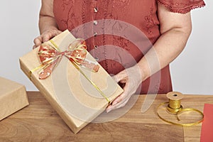 Unrecognizable woman wrapping a Christmas gift, neutral paper and festive ribbon