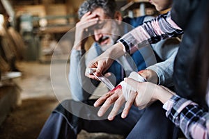 A woman bandaging a hand of a man worker after accident in carpentry workshop.