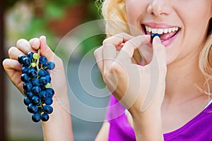 Unrecognizable young blond woman holding and eating blue grapes