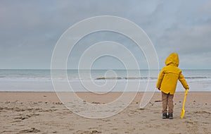 Unrecognizable young boy with bright yellow oilskin jacket on a deserted beach