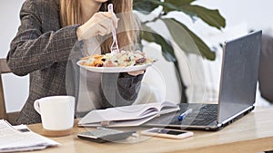 Unrecognizable young business woman having a lunch break at desk, she is eating fresh salad, person