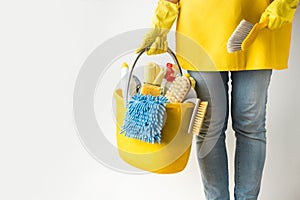 Unrecognizable young caucasian woman in a uniform wearing yellow rubber gloves and holding bucket full of cleaning supplies.