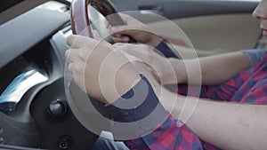 Unrecognizable young father teaching his son to drive the car close up. The boy sitting on father`s laps, both putting