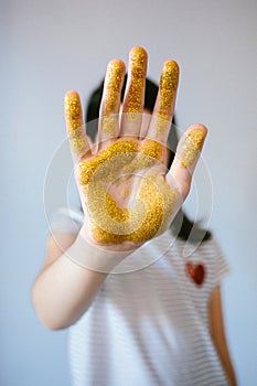 Unrecognizable young girl showing her palm hand covered of golden glitter while doing stop sign