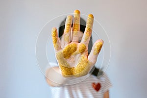 Unrecognizable young girl showing her palm hand covered of golden glitter while doing stop sign