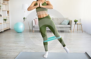 Unrecognizable young lady exercising with elastic band, working out her strength in living room