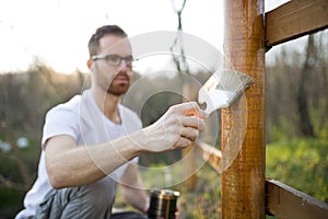 Unrecognizable young man painting wooden fence in backyard