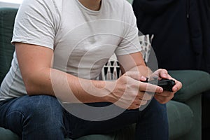 Unrecognizable young man playing video games with a gamepad sitting on sofa