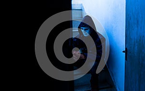 Unrecognizable young man white mask and hoodie sitting on old stairs,. Sadness, despair, dark, concept