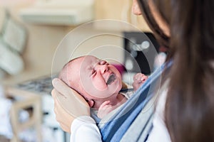 Unrecognizable young mother with her crying son in sling