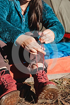 Unrecognizable young tourist woman sitting in the door of a camping tent and tying her red shoes
