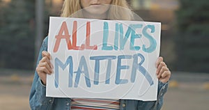 Unrecognizable young woman with All lives matter banner standing on urban city street. Strike of female Caucasian