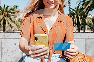 unrecognizable young woman buying online in a park with her phone and credit card photo