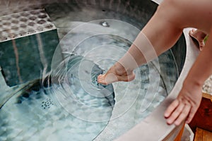 Unrecognizable young woman is dipping her foot in outdoor hot tub,trying temperature of water, spa, beauty and