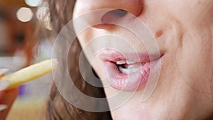 Unrecognizable young woman is eating french fries  in fast food restaurant. She is holding one hand potato, mouth closeup