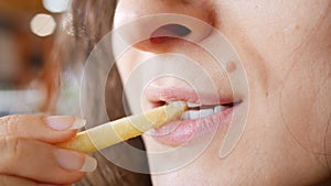 Unrecognizable young woman is eating french fries  in fast food restaurant. She is holding one hand potato, mouth closeup