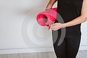 Unrecognizable Young woman listening holding yoga mat, ready to practice. Healthy lifestyle indoors