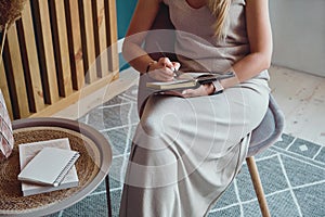 Unrecognizable Young woman making notes in notebook sitting at workplace at home, remote work