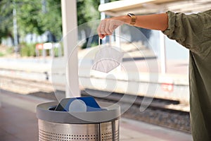 Unrecognizable young woman putting used dirty surgical mask into a garbage bin