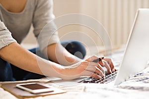 Unrecognizable young woman sitting on bed, working. Home office.