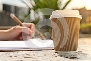 Unrecognizable Young woman study in beach resort. Drinking coffee from paper cup. Student making homework Female hands