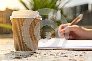 Unrecognizable Young woman study in beach resort. Drinking coffee from paper cup. Student making homework Female hands