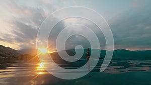 Unrecognizable young woman at summer sunset sea surfing on a SUP board.