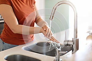 Unrecognizable Young Woman Washing Hands In Kitchen Sink