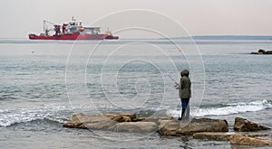 Unrecognized person standing on rocks fishing with rod on the sea in winter