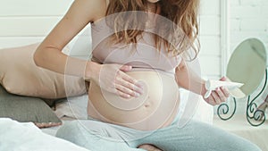 Unrecognized pregnant female carring belly with cream at home.