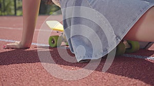 Unrecognized teen girl sits on a skateboard at outdoor basketball court in sunny summer weather. Concept of sport