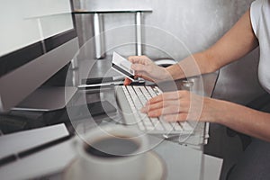 Unrecognized woman holding credit card in hand and using laptop computer keyboard.
