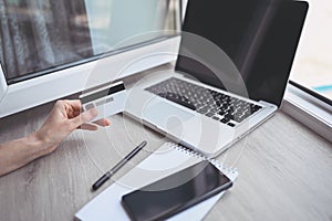 Unrecognized woman holding credit card in hand and using laptop computer keyboard.